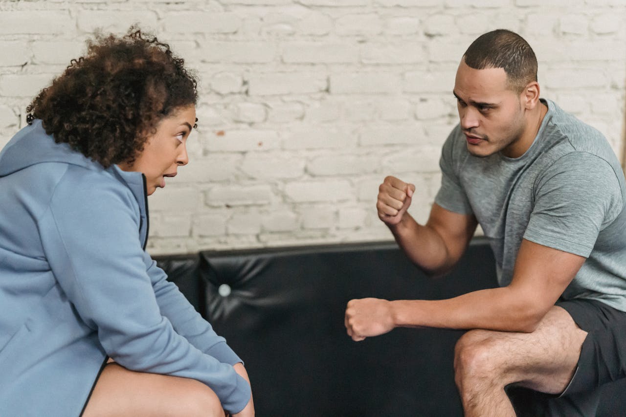 Side view of sportive black personal trainer showing technique of exercise to African American woman while looking at each other in gym